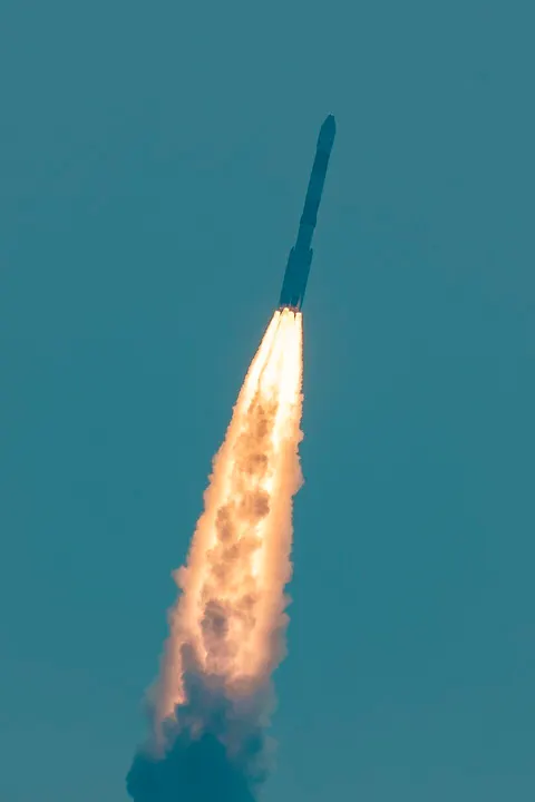 A rocket climbing steeply into a clear sky, trailing a bright orange flame and a thick plume of smoke.