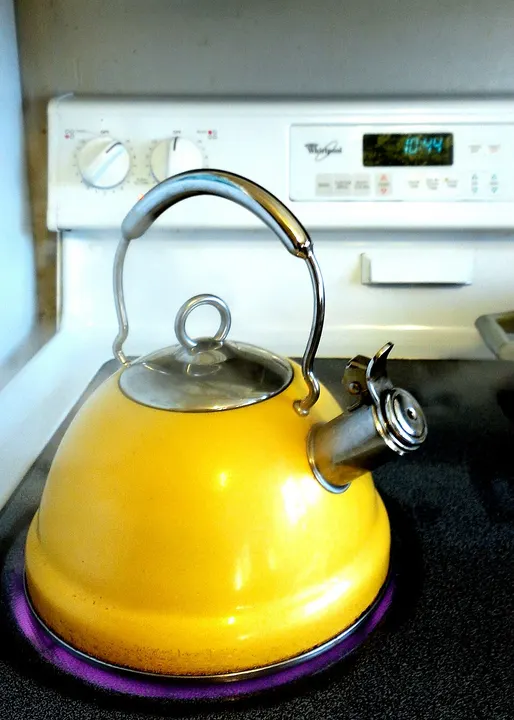 A shiny yellow kettle with a steel handle and spout sitting on a stove burner.