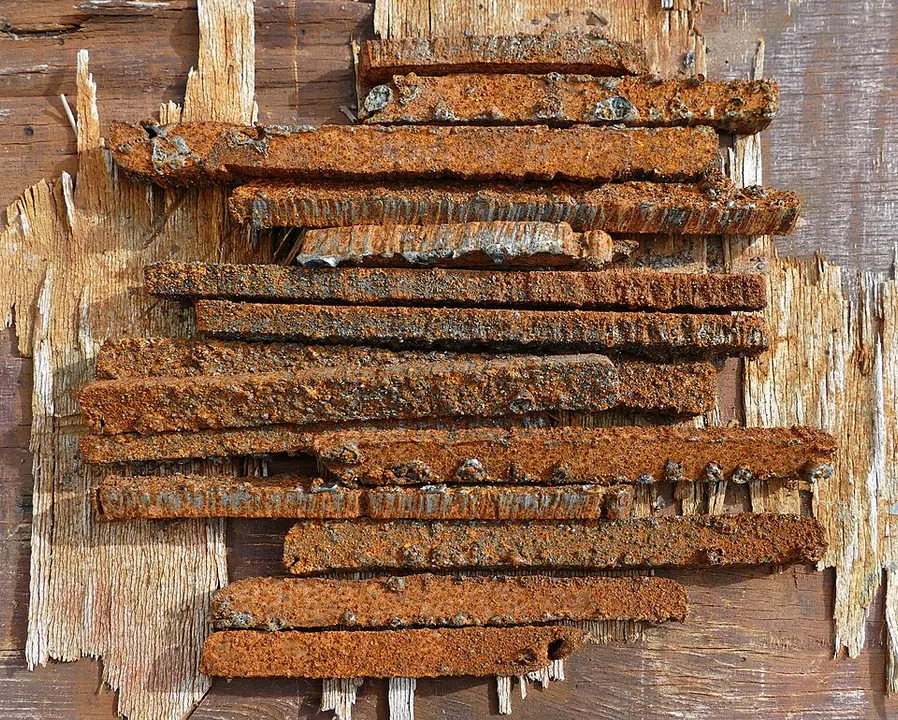 A stack of flat rusty orange-brown iron strips lying on weathered wooden boards.