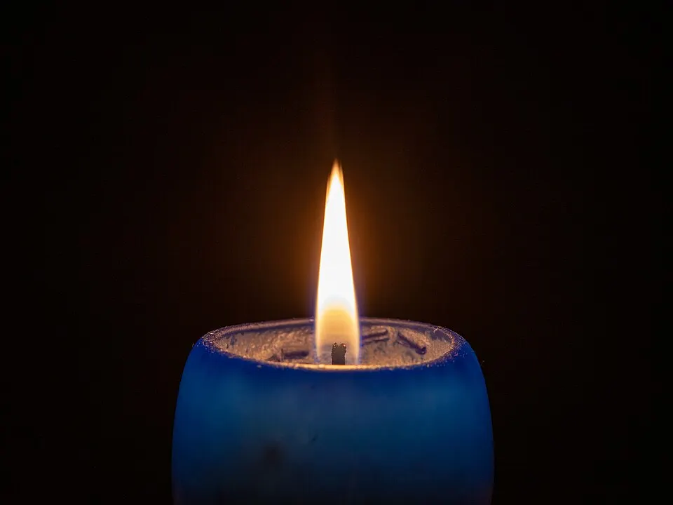 A single bright candle flame burning on top of a blue candle against a black background.