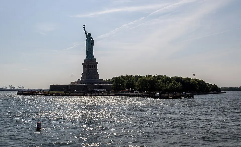 A large green statue of a robed woman raising a torch, standing on a stone base on an island.