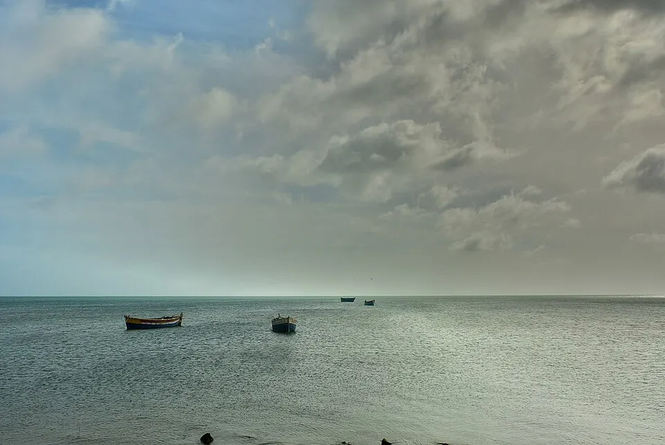 Small wooden boats floating on a calm grey sea under heavy clouds.