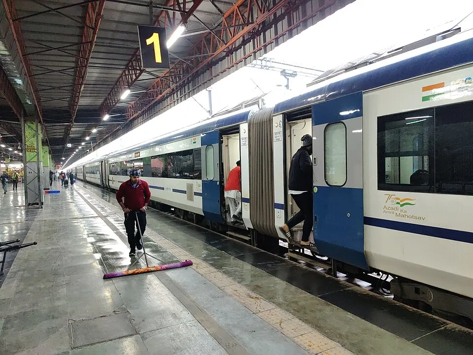 A long white and blue passenger train standing at a busy railway platform.