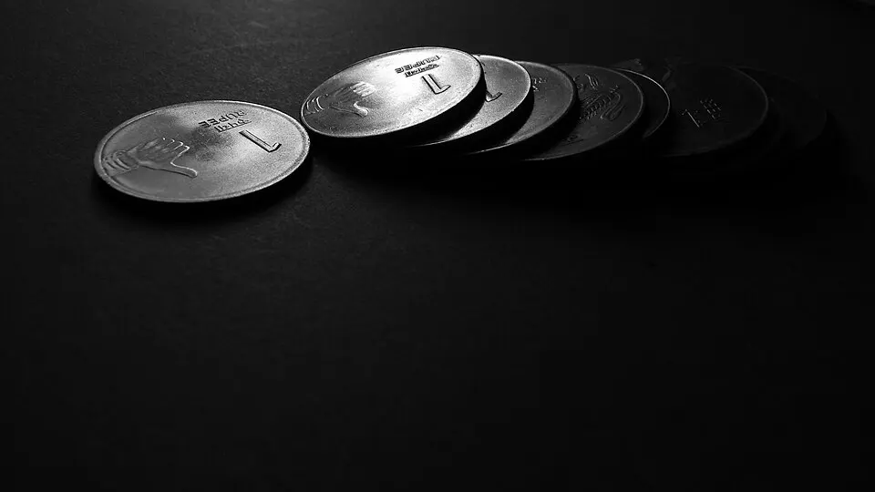 A row of silver coins lying on a dark surface.