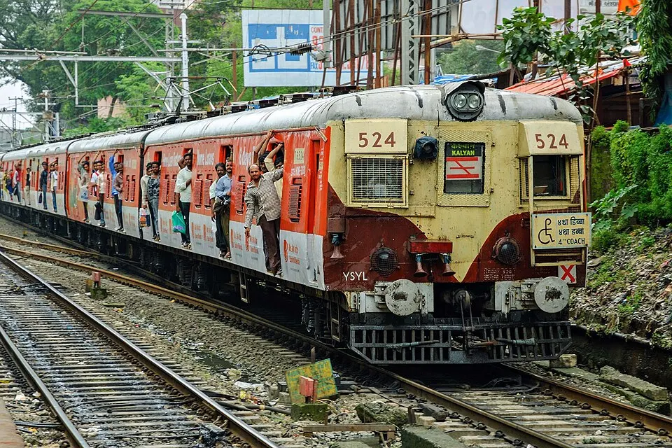 A yellow-and-red suburban train rounds a bend with passengers leaning out of its open doors.