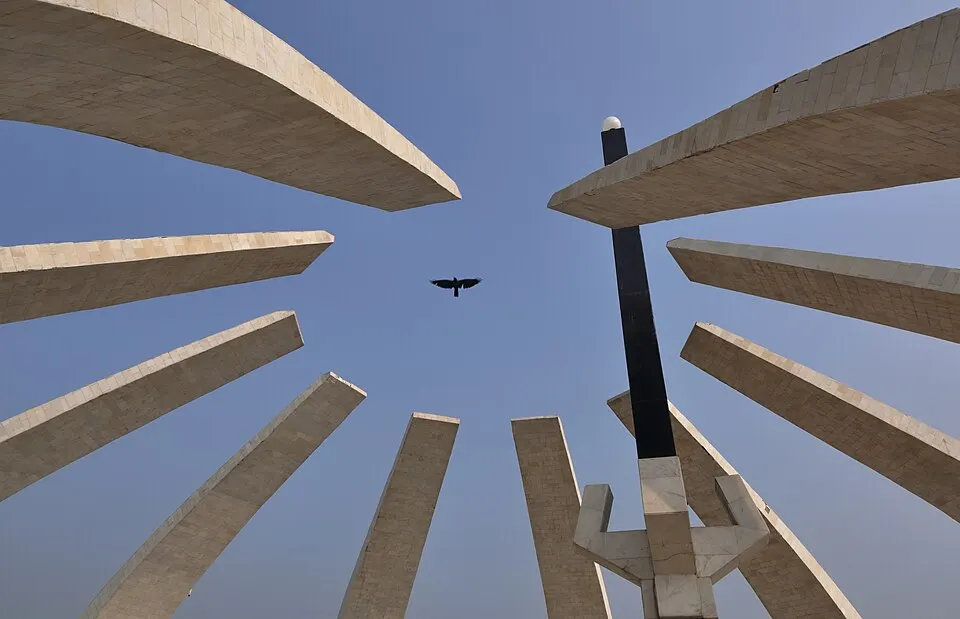 Tall pale stone ribs of a monument curve upward against a clear blue sky as a crow flies overhead.
