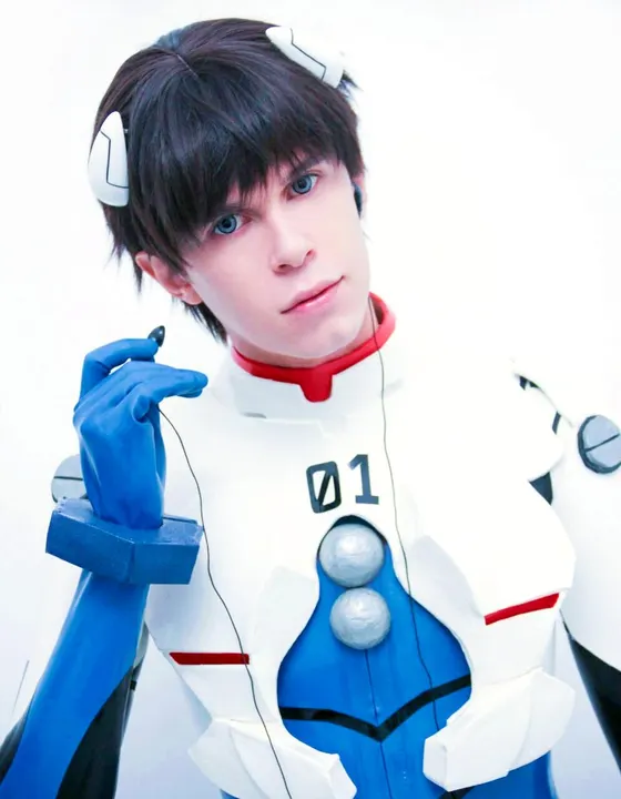 A cosplayer in a white and blue bodysuit with a red collar and the number 01, holding an earphone wire, against a white backdrop.