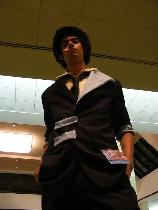 A cosplayer in a dark suit with a loose tie and a cigarette in the mouth, photographed from a low angle indoors.