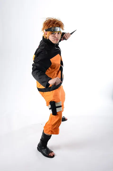 A cosplayer in an orange and black tracksuit, spiky orange wig and metal forehead headband, striking a pose with a kunai.