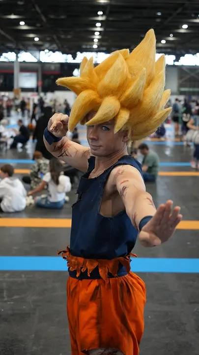 A cosplayer with a spiky golden wig, torn dark blue top and orange trousers, holding one hand out in a fighting pose.