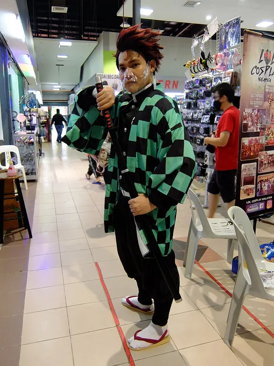 A cosplayer with dark red hair in a green and black checkered haori, holding a sheathed sword in a shopping-mall corridor.