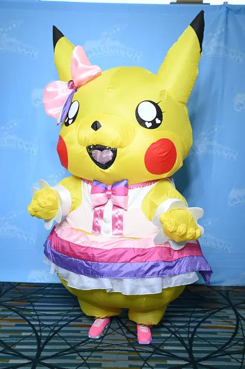 A person in an inflatable yellow costume with black-tipped ears, a pink bow, a frilly dress and pink shoes in front of a blue backdrop.