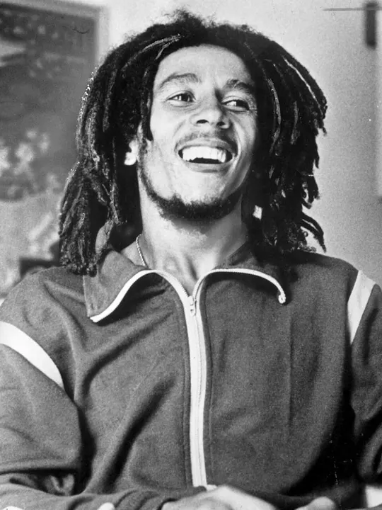 A man with dreadlocks performing on stage with a guitar.