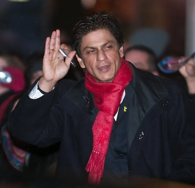 A man in a red scarf and dark coat waving to a crowd at night.