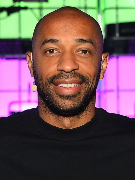 A tall former striker in a dark coat at a media event.