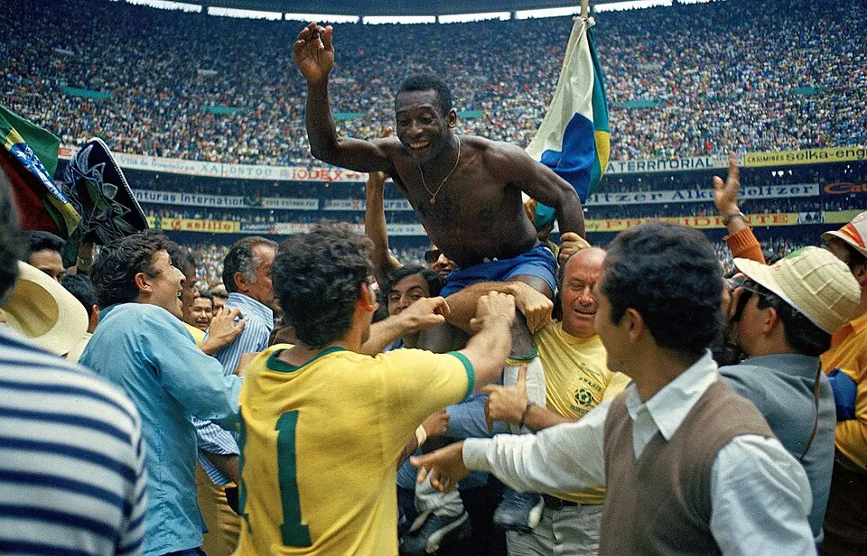 A footballer in a yellow shirt carried shoulder-high by a celebrating crowd.