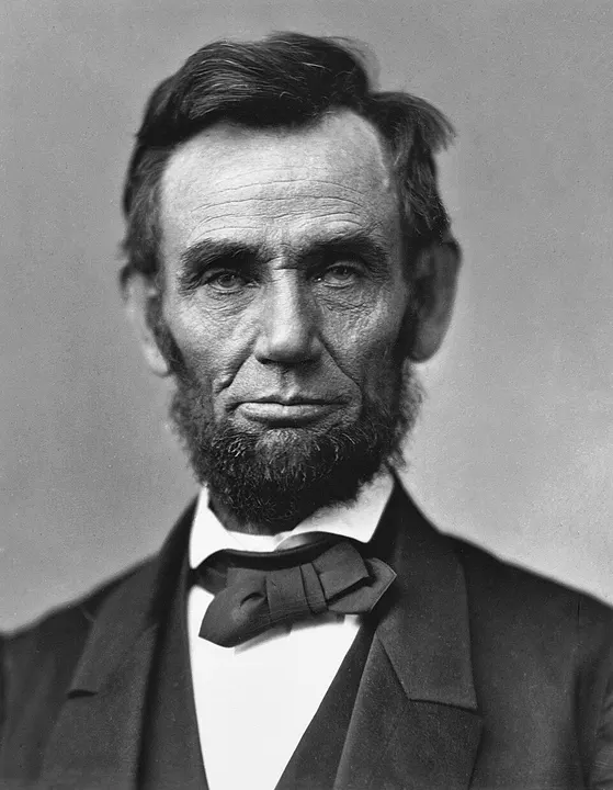 A black-and-white portrait of a tall bearded man in a dark suit.