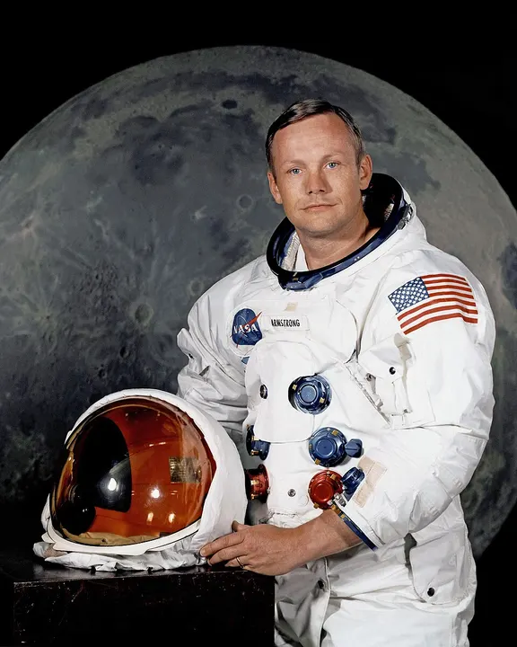 An astronaut in a white spacesuit holding a helmet.