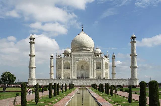 White marble mausoleum with a large central dome and four minarets, behind a long water channel and gardens