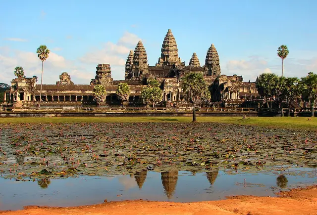 Temple with several tall towers reflected in a pond, palm trees around it