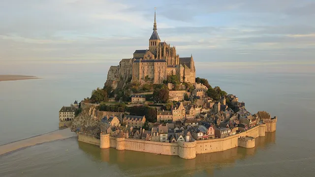 Aerial view of a rocky island crowned by an abbey spire, surrounded by water and sand
