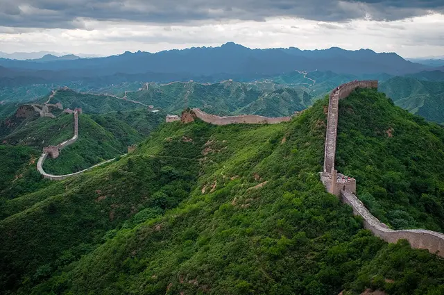 Stone wall with watchtowers winding along green mountain ridges