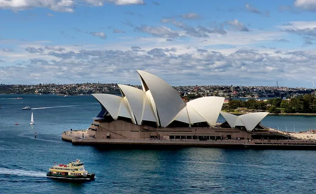 White shell-like roofs of a building on a harbour, with a ferry passing in front