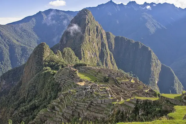 Stone ruins and farming terraces on a ridge below a steep green peak