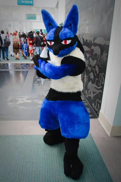 A person in a fluffy blue and black furry costume with red eyes, a cream chest and spikes on the paws.