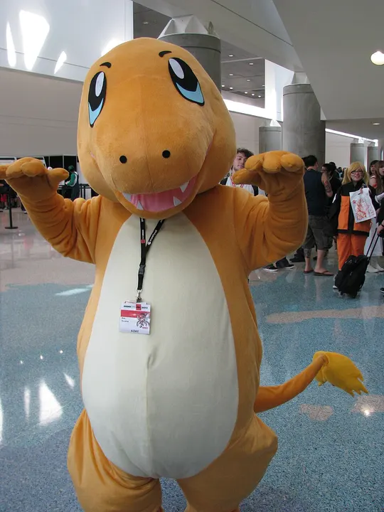A person in an orange mascot costume with big blue eyes, a cream belly and a yellow-tipped tail in a convention hall.