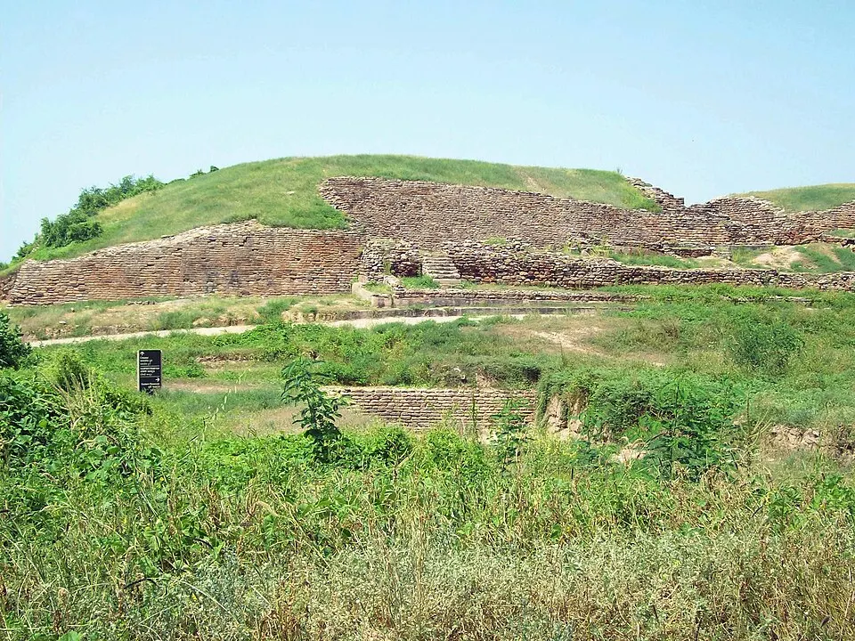 Stone and brick fortification walls climb a grassy mound with bushes in the foreground.