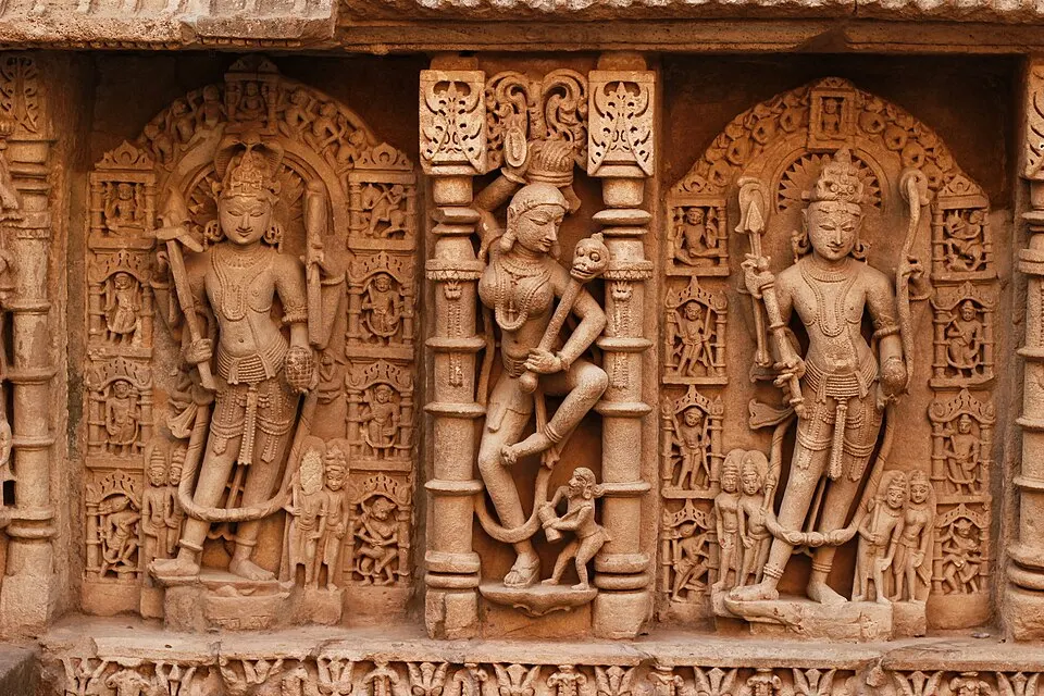 Rows of intricately carved stone figures stand in niches on a sandstone wall.