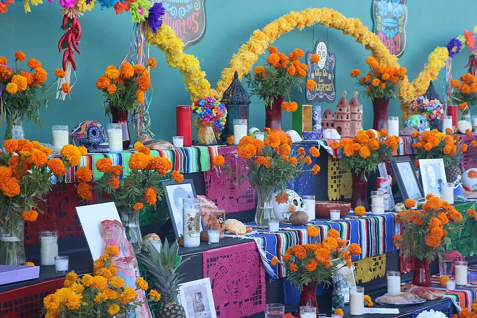 A multi-tiered display covered in orange marigolds, candles, framed photos, sugar skulls and colourful paper banners.
