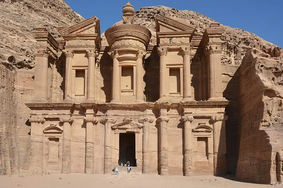 A huge rock-cut building with tall columns carved into a pink sandstone cliff.