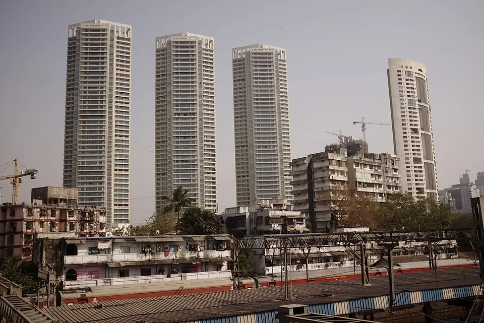 Several tall residential towers rise above older low buildings and railway tracks under a hazy sky.