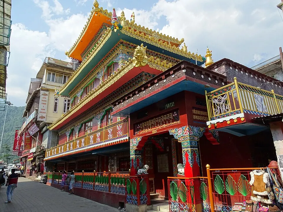 A brightly painted multi-tiered Tibetan-style temple with golden roof ornaments stands on a narrow hill-town street.