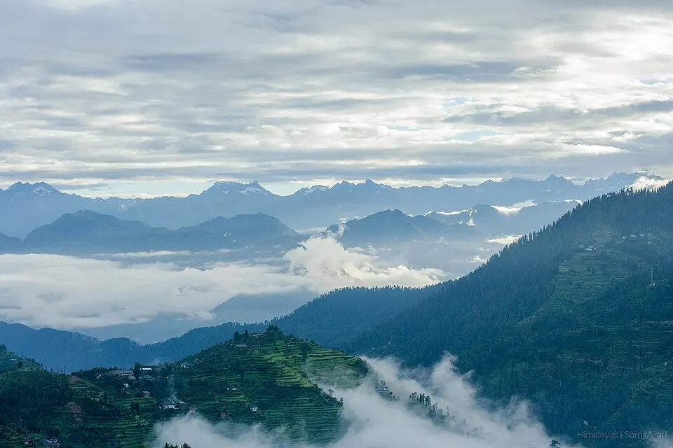Layers of misty blue mountain ridges rise above clouds and green terraced hillsides.