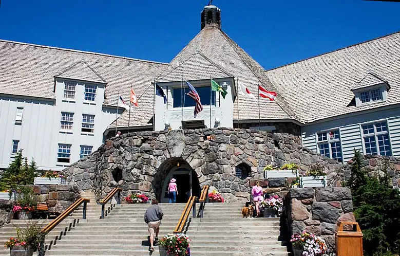 A big mountain lodge with steep shingled roofs, flags and a stone archway entrance with steps.