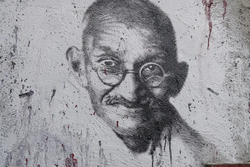 A black and white stencil portrait of a bald man with round glasses painted on a rough white wall.