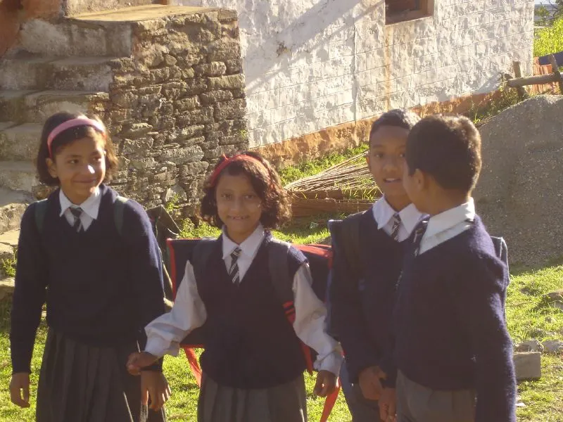 Smiling schoolchildren in navy sweaters, ties and backpacks standing outside a stone building.