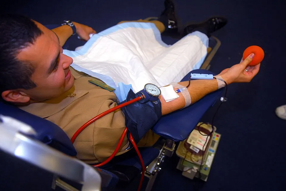 An adult man sitting in a medical chair with a tube running from his arm to a collection bag while he squeezes a ball.