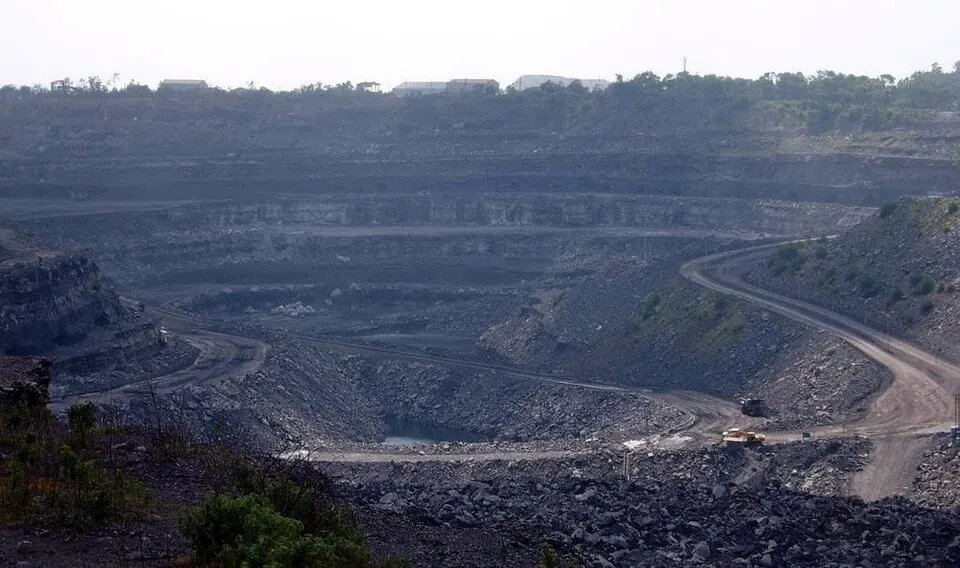 A vast open-cast mine with dark stepped terraces and winding haul roads, with a couple of trucks in the pit.