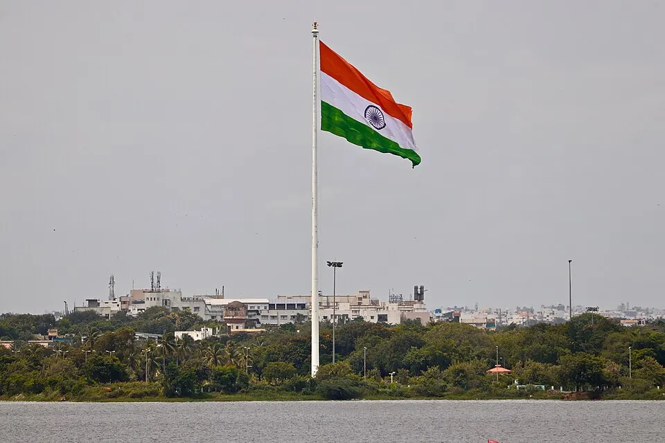 झील के किनारे एक ऊँचे खंभे पर लहराता केसरिया, सफ़ेद और हरे रंग का झंडा, जिसके बीच में नीला चक्र है।