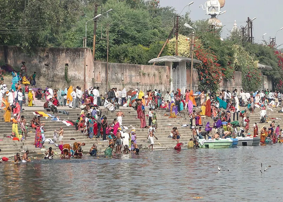 Crowds of people in colourful clothes bathe and gather on broad stone steps leading down to a river.