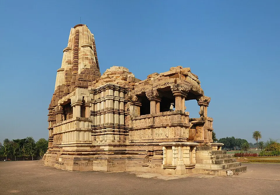 A sandstone temple with a tall curved spire and an open pillared porch stands on a raised platform under a clear blue sky.