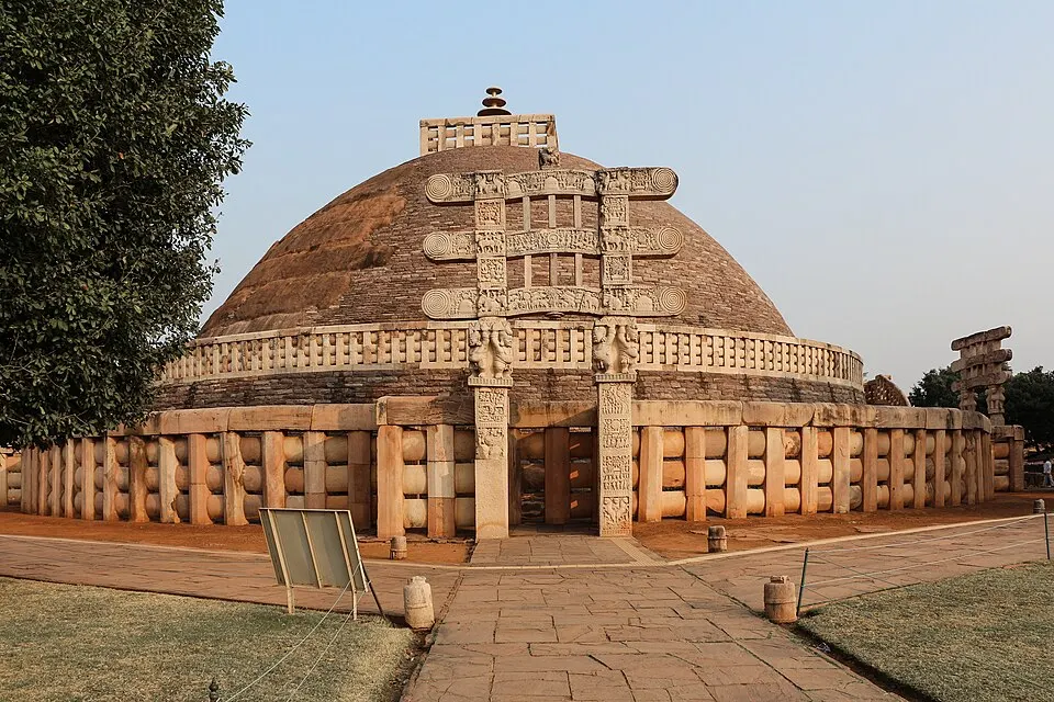 A large hemispherical stupa ringed by a stone railing has a carved stone gateway in front of it.