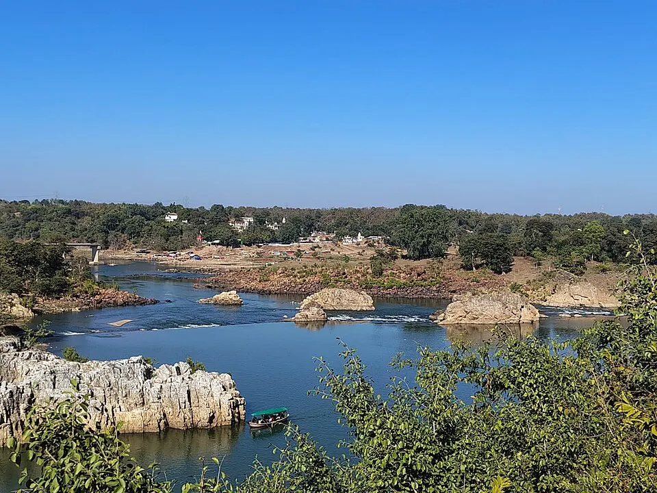 A wide blue river winds between pale rocky outcrops and green trees, with a small boat on the water.