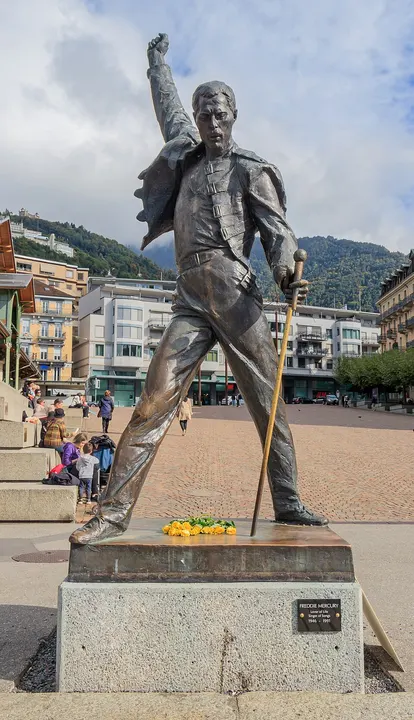 A bronze statue of a singer with one fist raised and a microphone stand in hand, standing in a plaza with mountains behind.