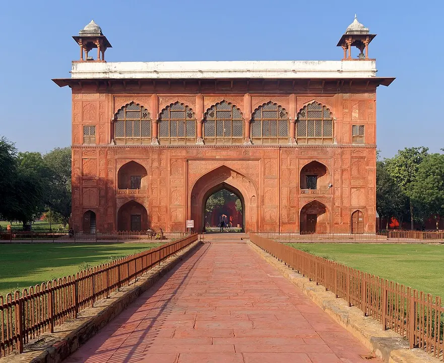A red sandstone gatehouse with arched windows and small domed pavilions on its roof, at the end of a paved path.