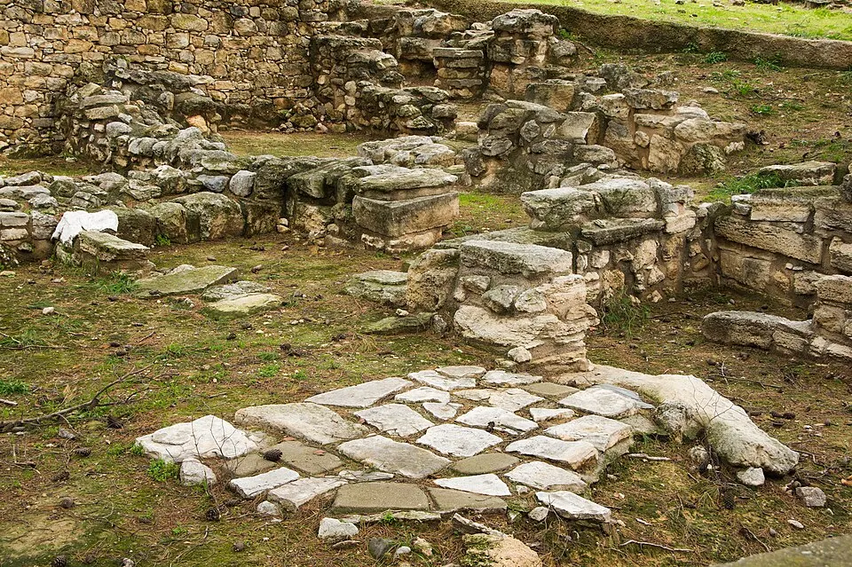 Ancient stone ruins with low walls and a patch of flat paving slabs in the foreground.